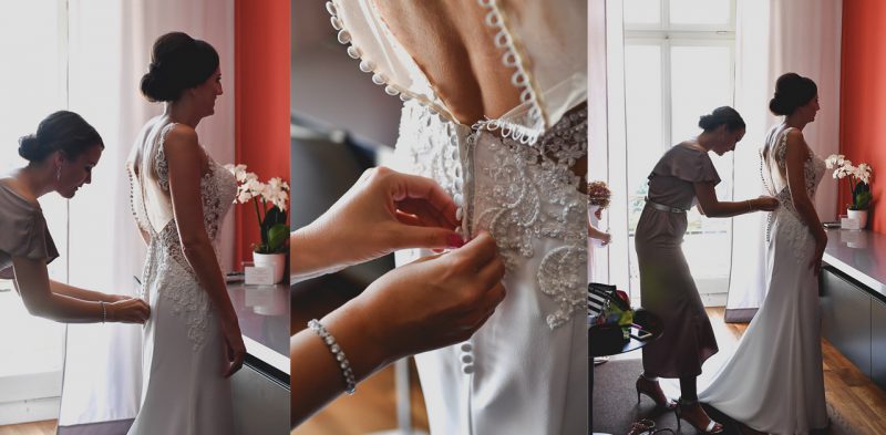 Die Braut schluepft in ihr Brautkleid und der Hochzeitsfotograf macht die Bilder.